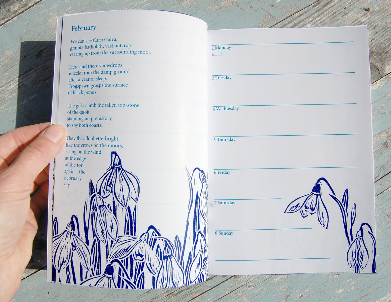 Open book with blue floral illustrations and a calendar on a wooden surface