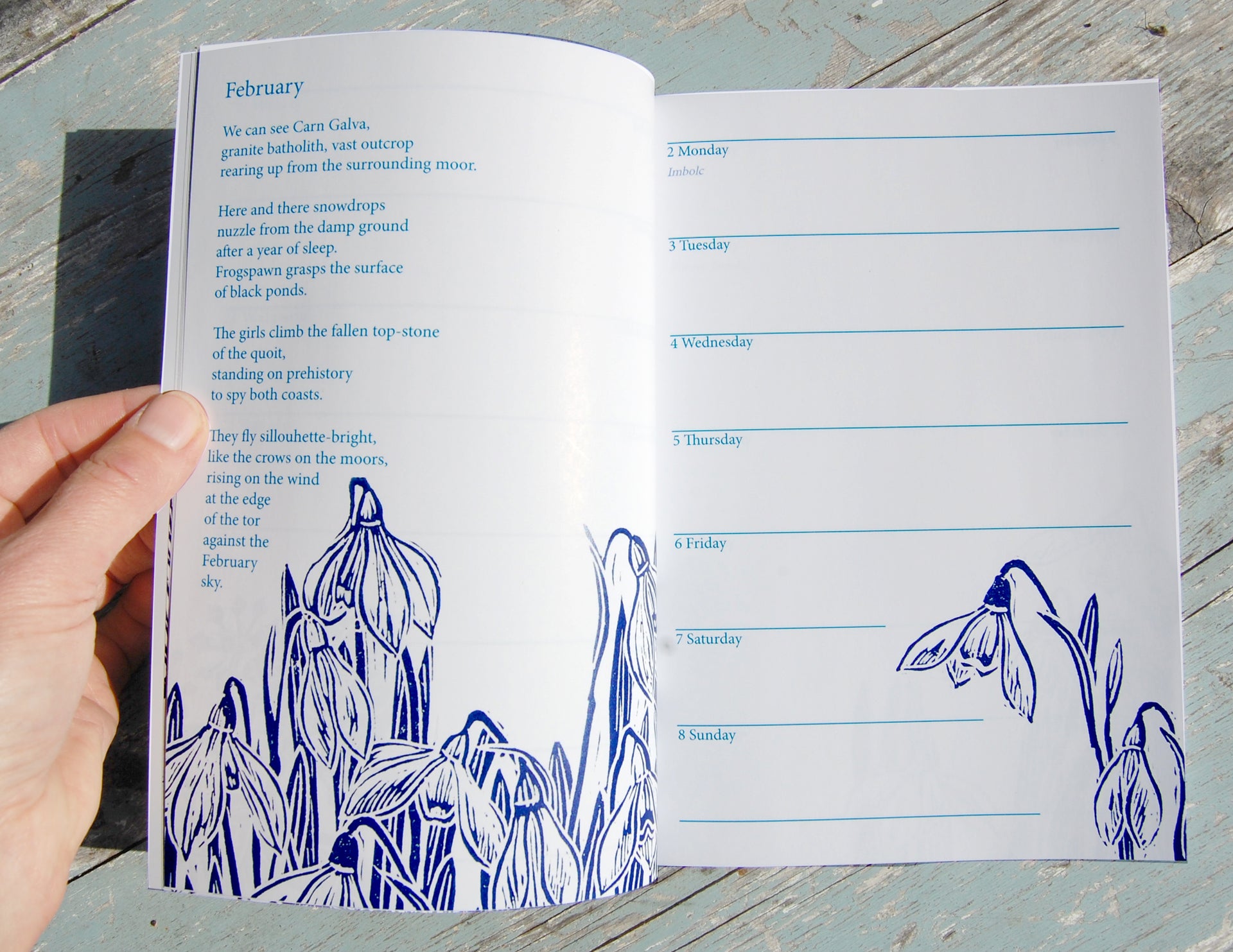 Open book with blue floral illustrations and a calendar on a wooden surface
